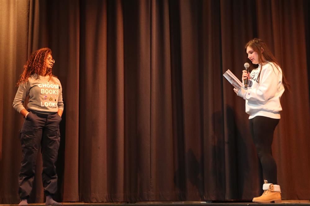 A student speaking on stage to an author A student speaking on stage to an author